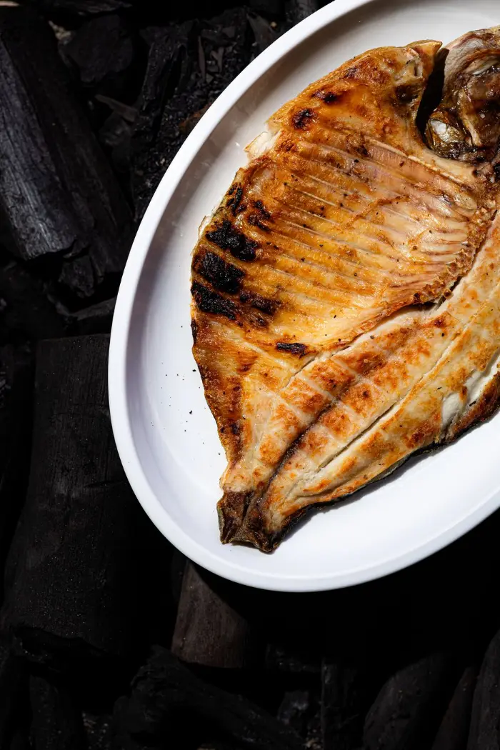 Peixe aberto na chapa, pele crocante, no prato branco sobre carvão