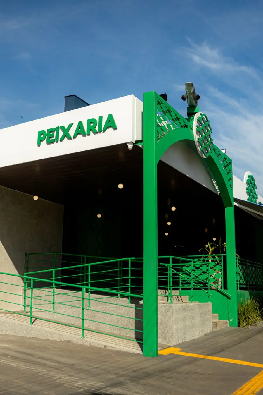 Entrada da peixaria com arco verde, rampa e luminárias quentes