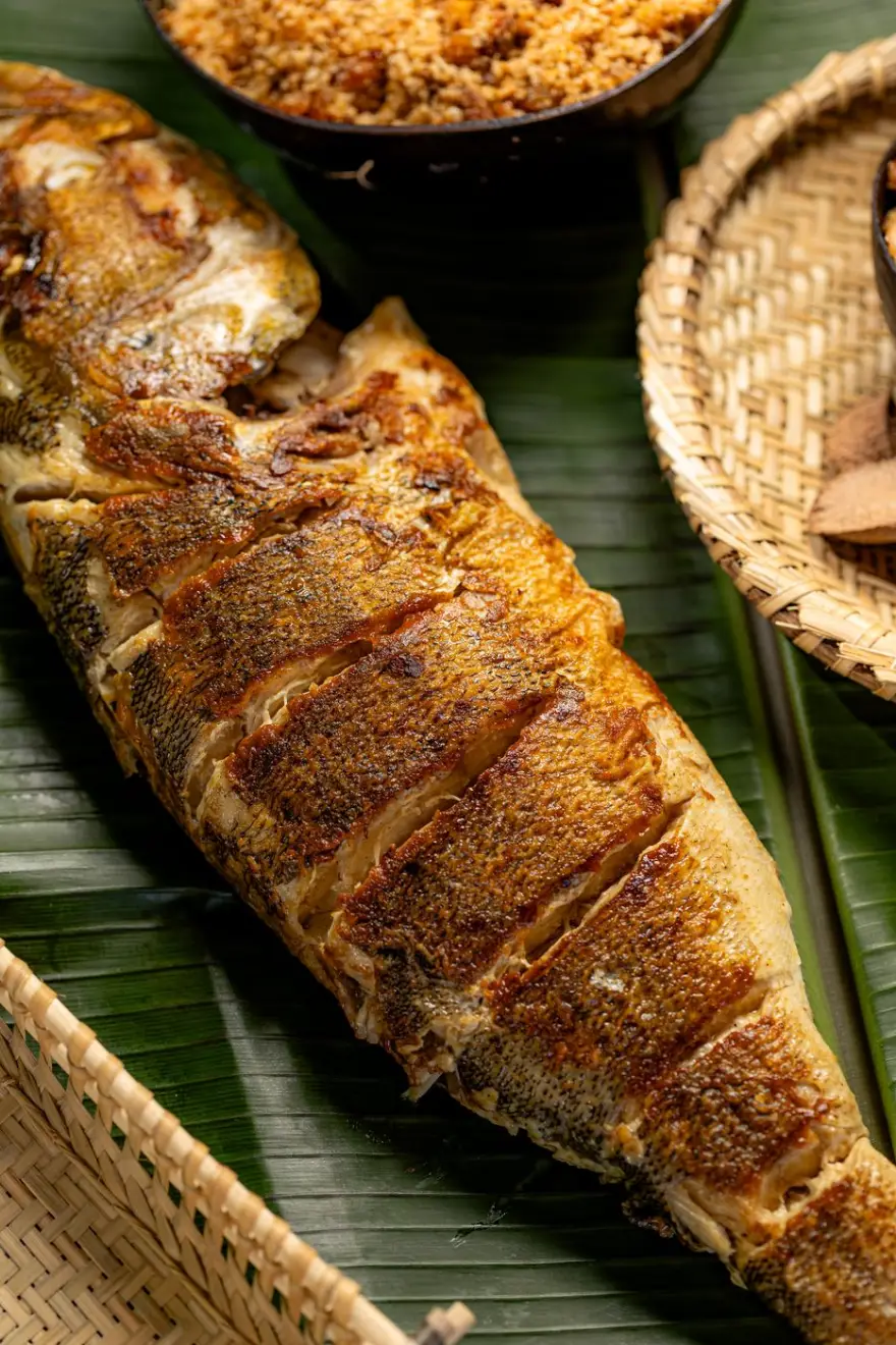 Peixe inteiro grelhado servido sobre folha de bananeira, com farofa